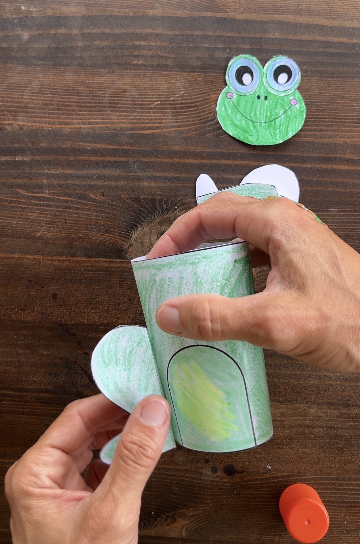 gluing the right leg on a paper frog craft
