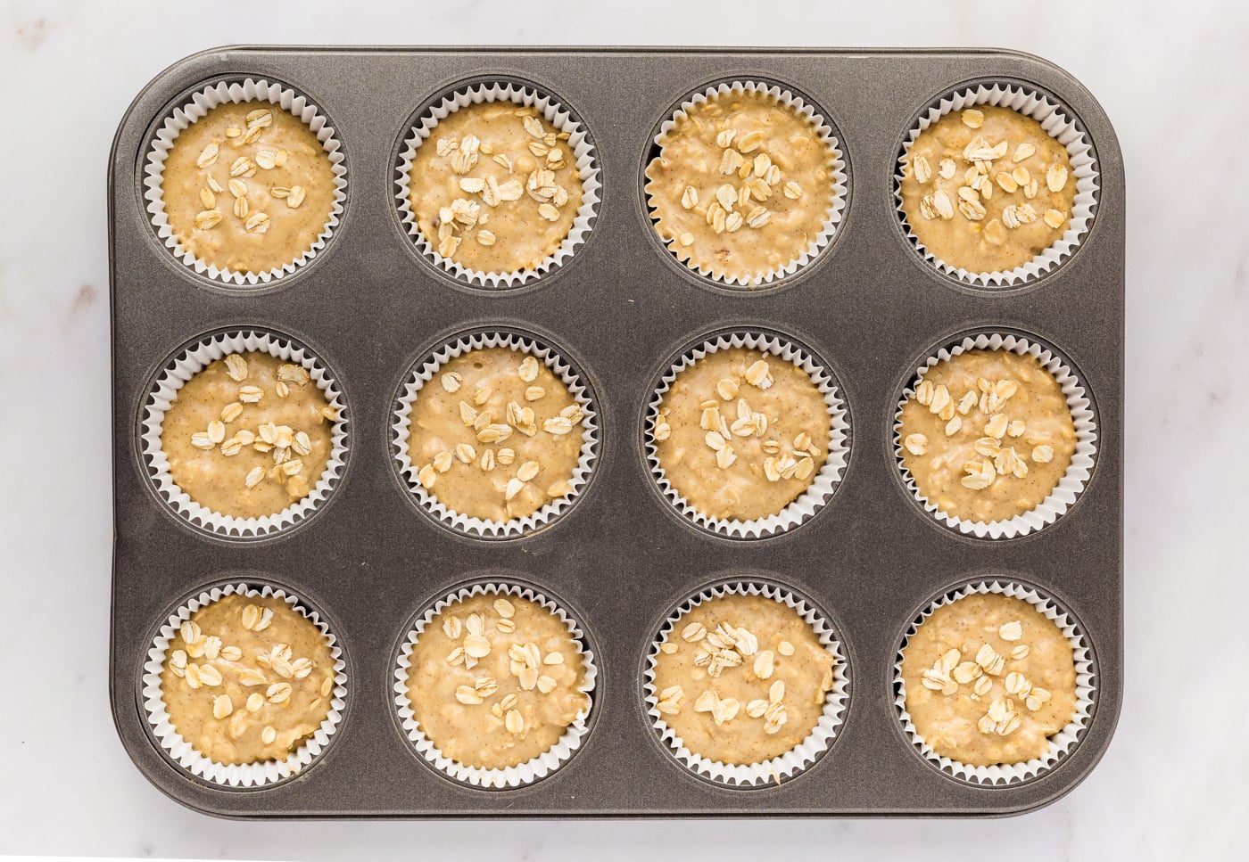 a top down photo of a tray of 12 unbaked gluten free oatmeal muffins