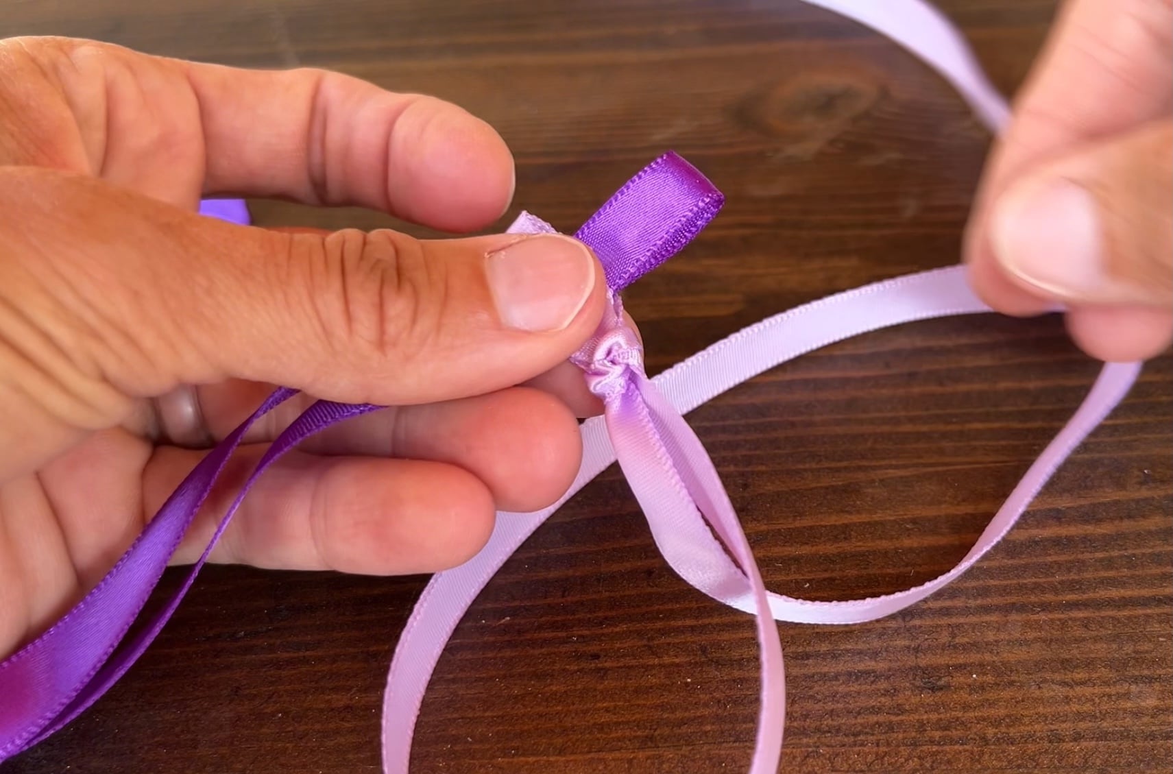 passing a loop of purple ribbon through slip knot in a. lighter piece of ribbon