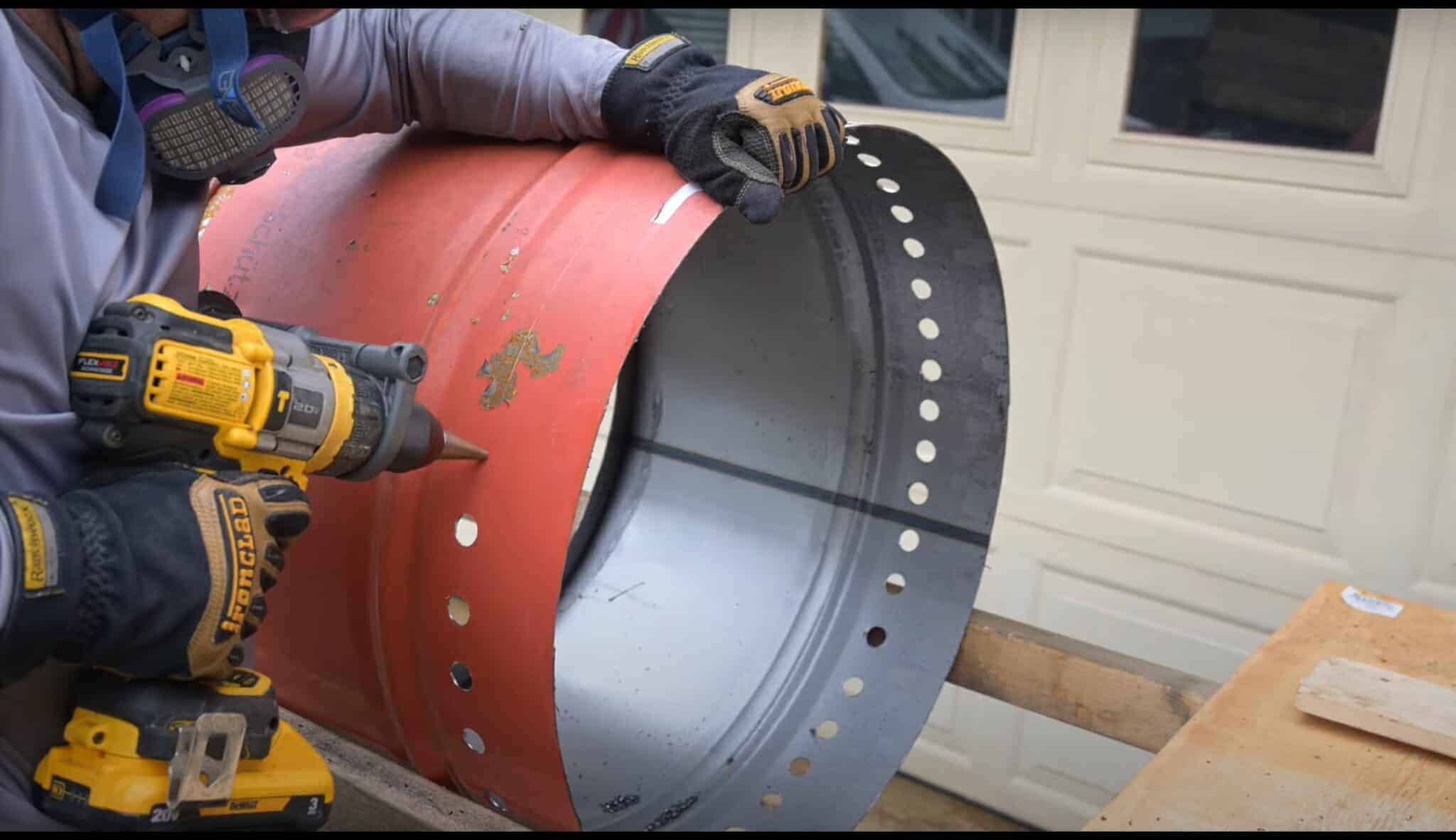 Photo is of a man drilling ¾" holes from the outer shell of a 55 gallon drum firepit.