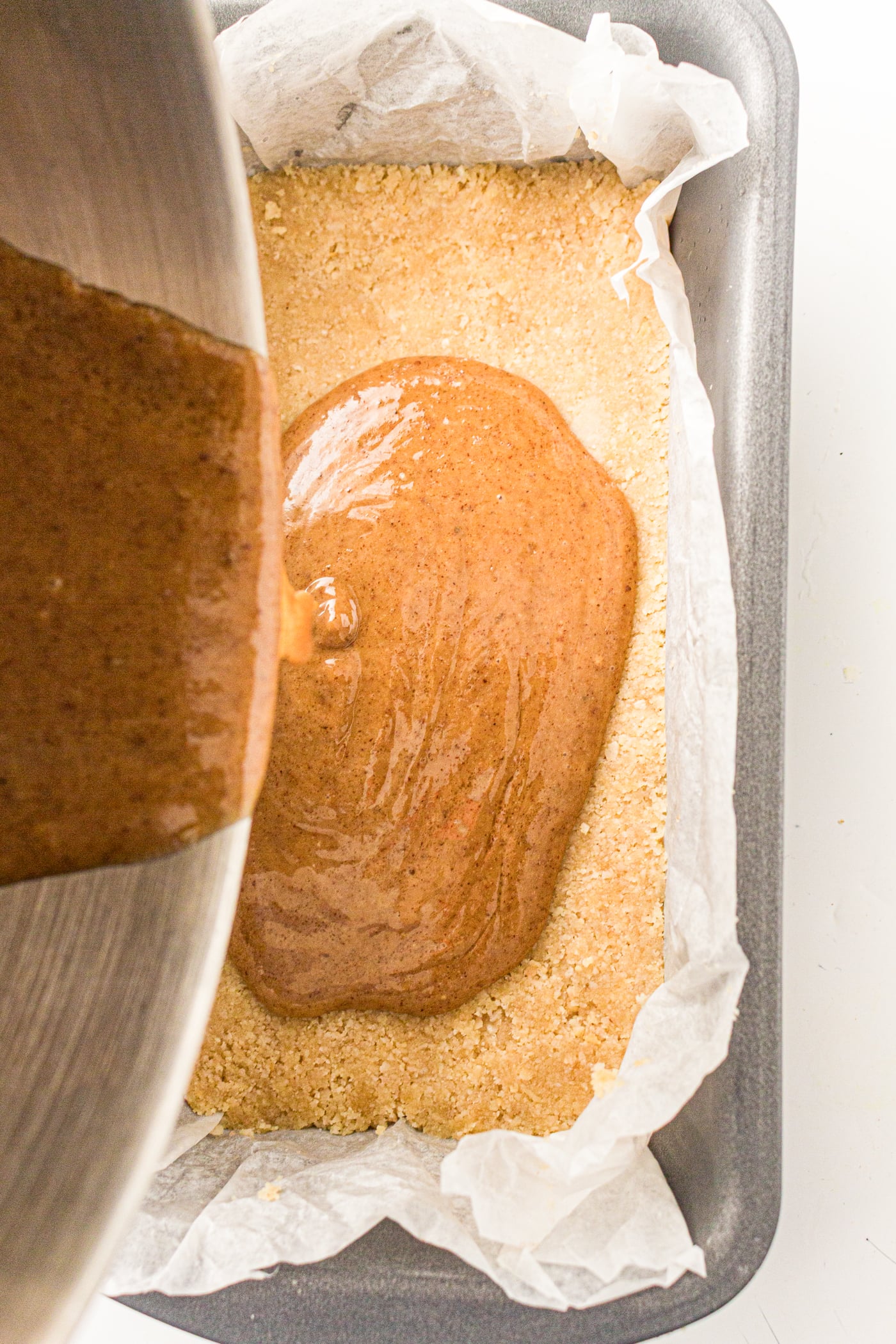 pouring almond butter mixture onto a base layer to make gluten free copycat twix bars
