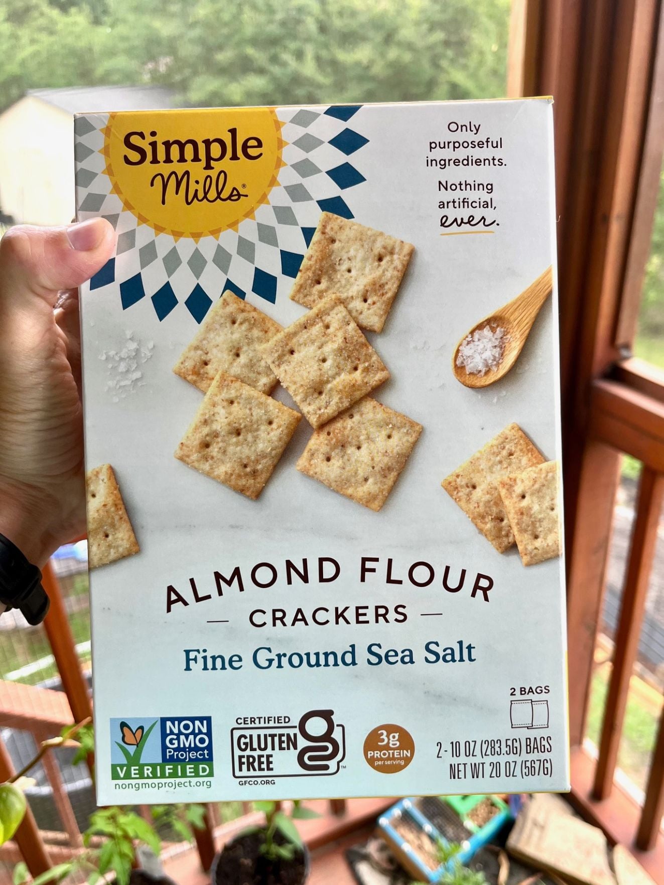 a woman's hand holding a box of simple mills almond ground crackers
