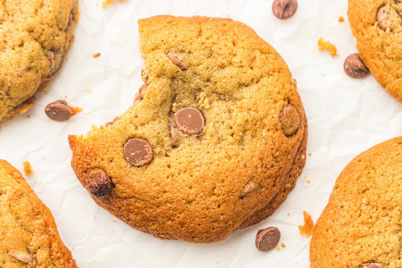 a bakery style sourdough discard chocolate chip cookie on parchment paper. It has a bite taken out of it.