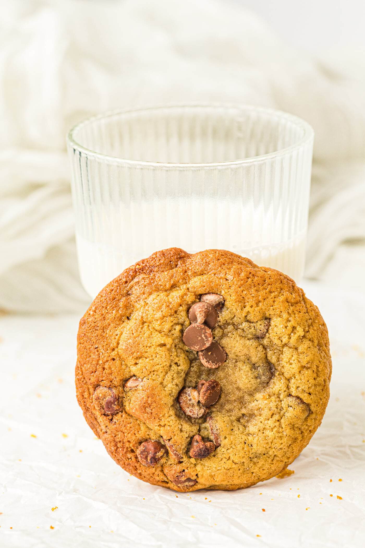 a chocolate chip cookie in front of a glass of milk