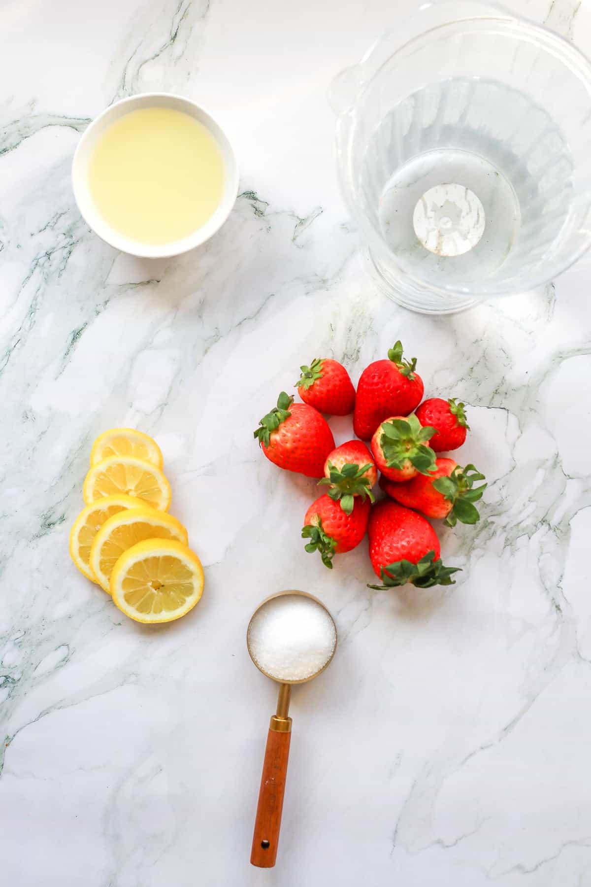 ingredients for strawberry lemonade including a pitcher with water, lemon juice, lemons, and strawberries