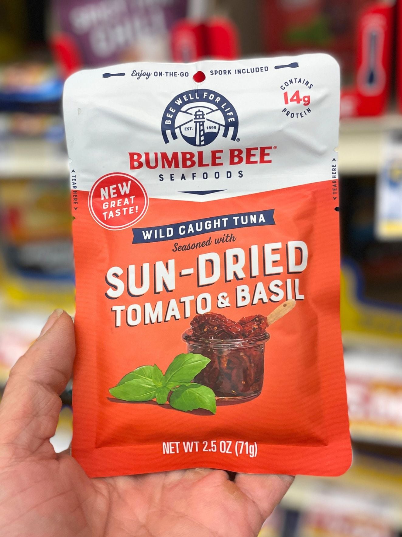 a hand holding a pouch of sun dried tomato basil flavored tuna