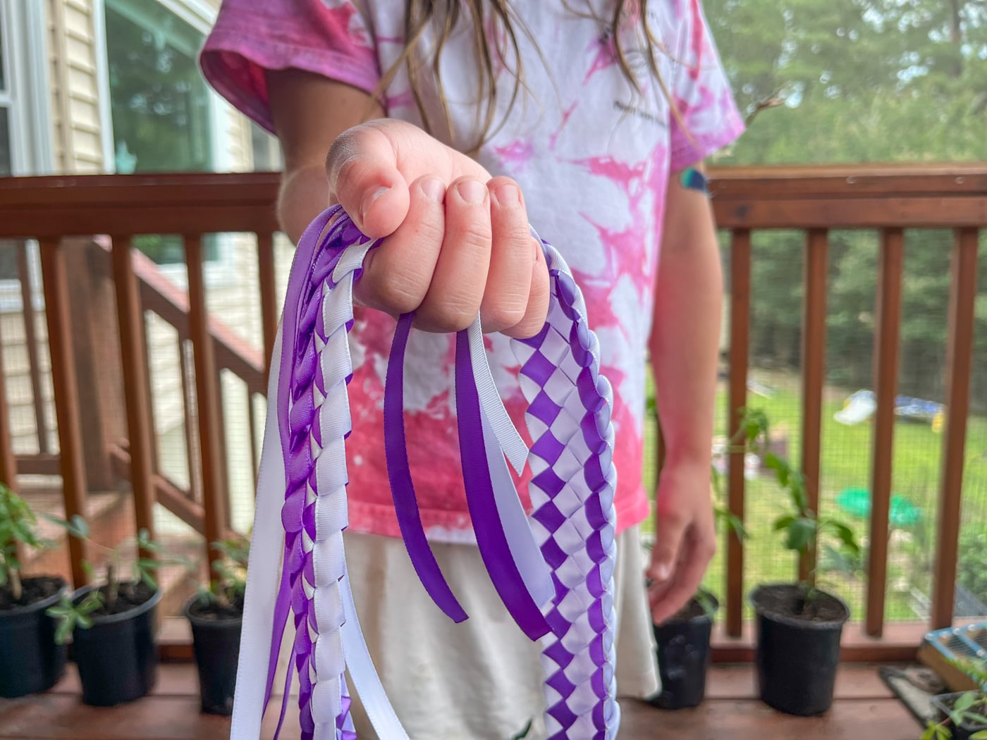 a child holding out a purple and white ribbon lei to give as a gift