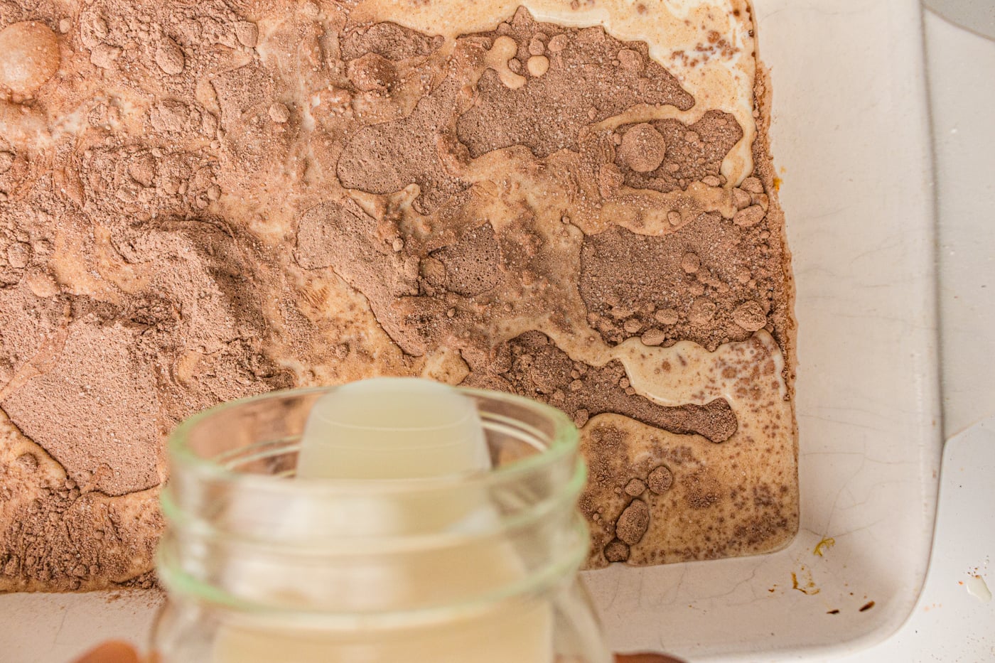 adding wet ingredients to a chocolate dump cake in a pan