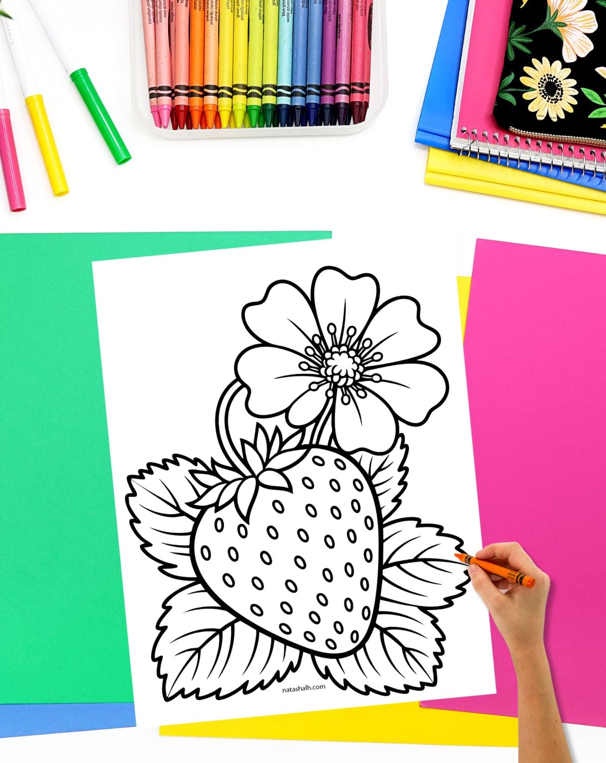 a hand with a crayon preparing to color a realistic strawberry coloring page featuring a strawberry and a strawberry blossom with leaves