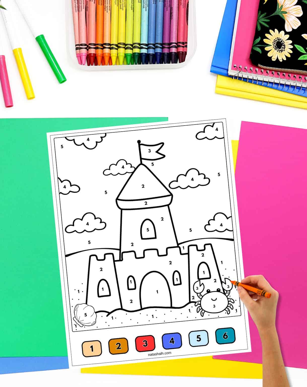 a child's hand with a crayon preparing to color a sandcastle color by number sheet