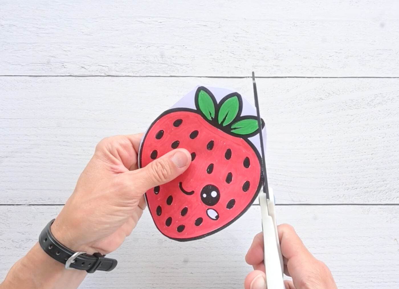cutting out around the leaves of a paper strawberry