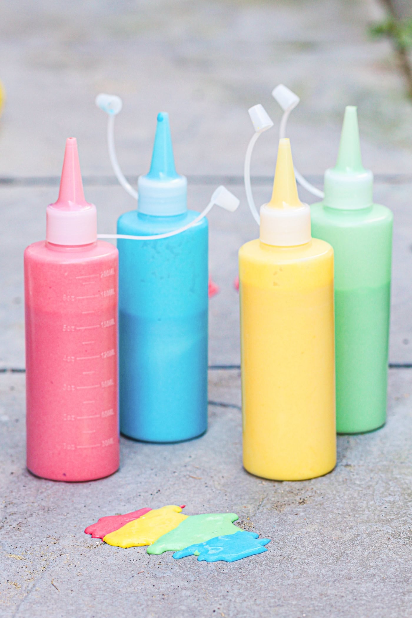 four bottles of DIY puffy sidewalk paint on the sidewalk in front of a small rainbow design