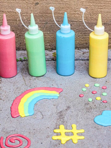 four bottles of sidewalk puff paint in squeeze bottles on the sidewalk in front of a rainbow, dots, a heart, a spiral, and a hash sign made with the puff paint