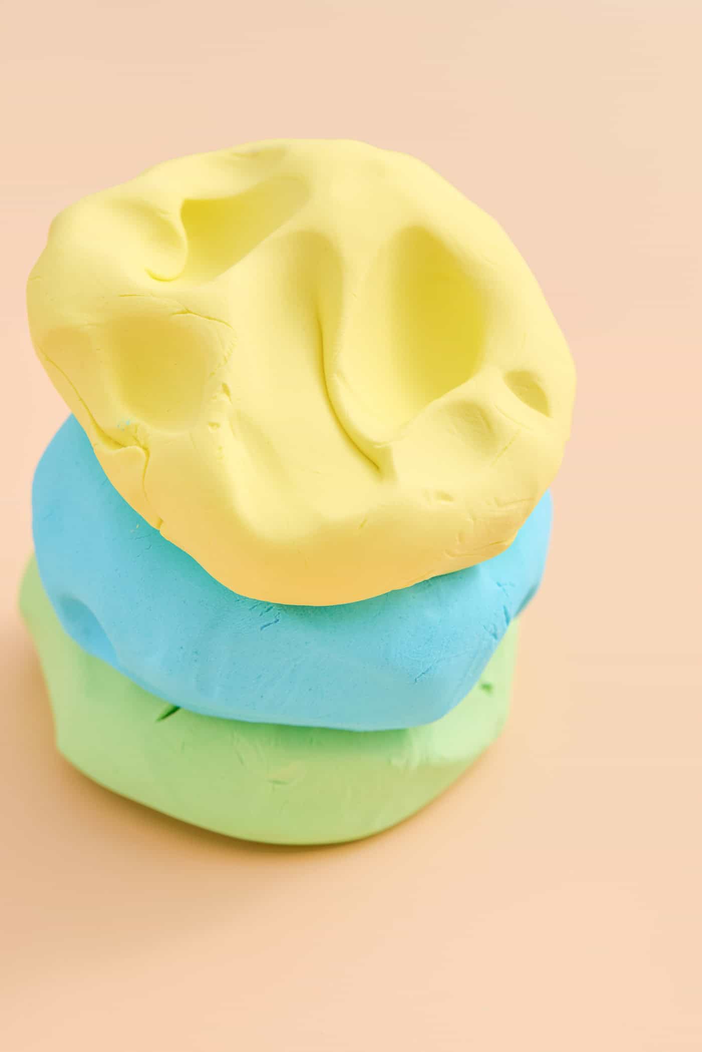 a stack of three colors of homemade cloud dough on a peach colored background