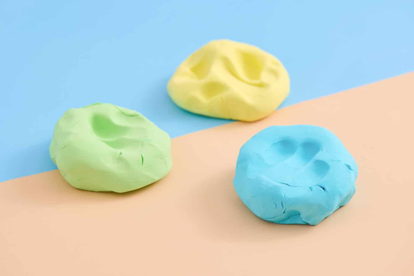 three balls of homemade cloud dough on a. blue and peach colored background