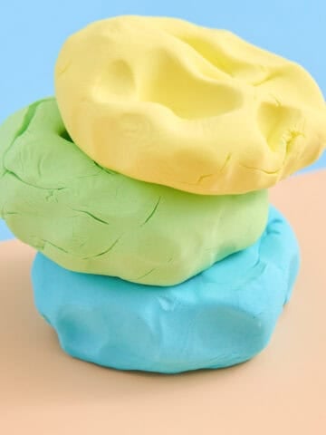a stack with three colors of homemade cloud dough on a peach and blue background
