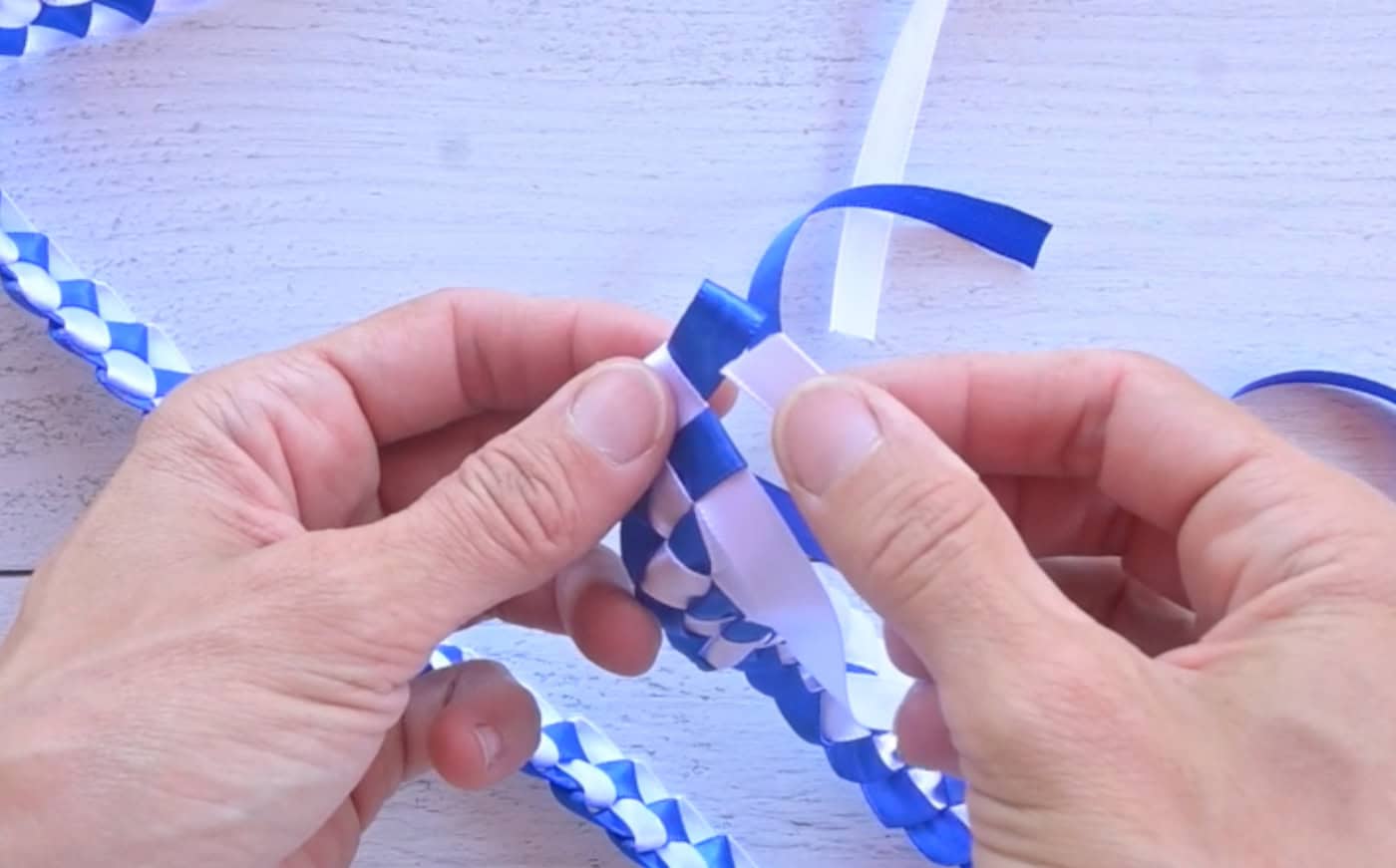 sending a piece of white ribbon through a blue ribbon loop to finish off a ribbon lei