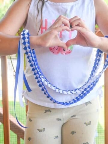 a child holding a blue and white braided Hawaiian ribbon lei