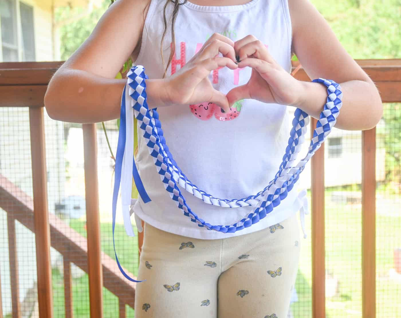 a child making a heart shape with her hands and holding a blue and white braided ribbon lei