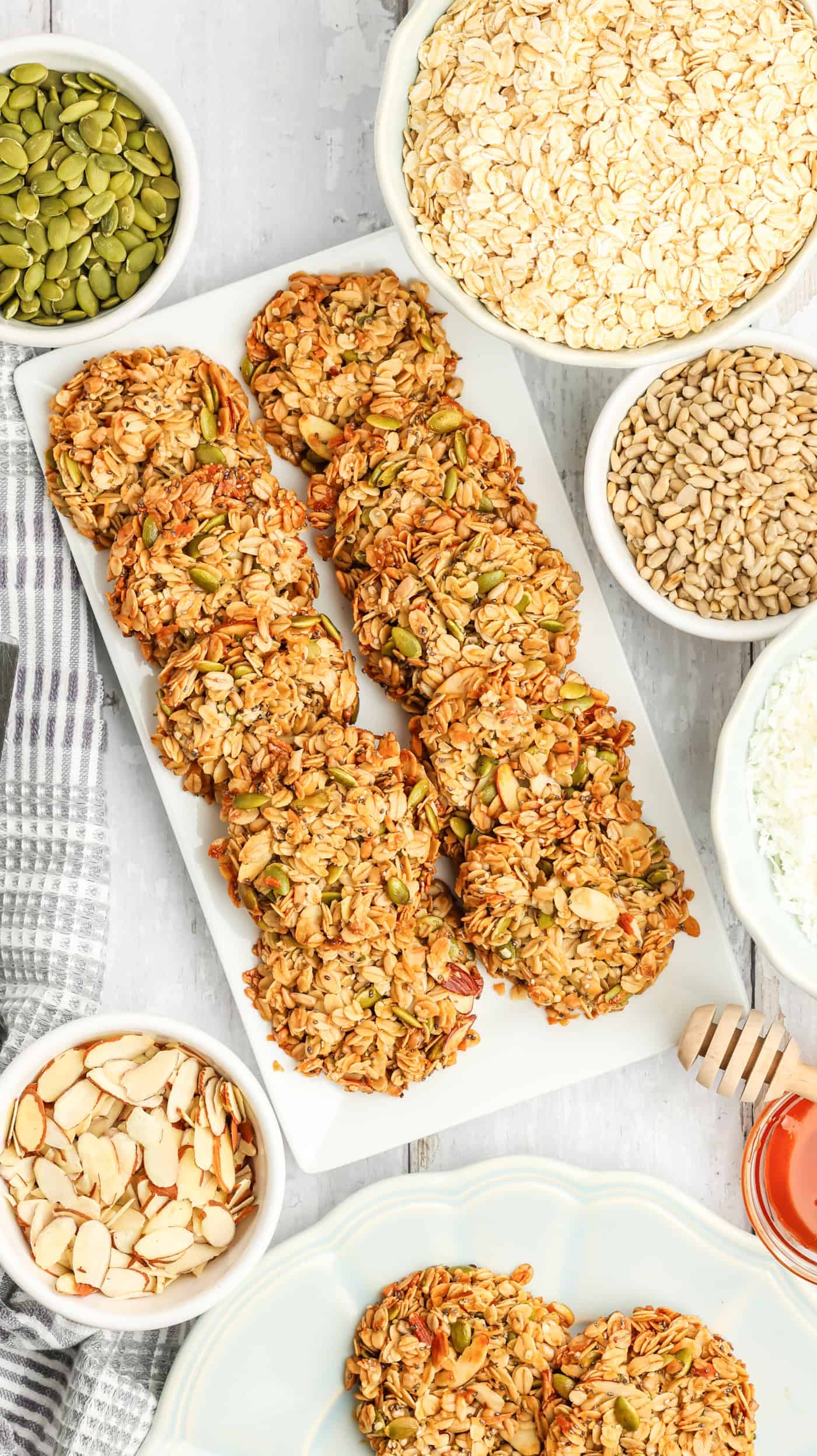 a top down photo of a plate of granola cookies surrounded by oatmeal, nuts, and seeds