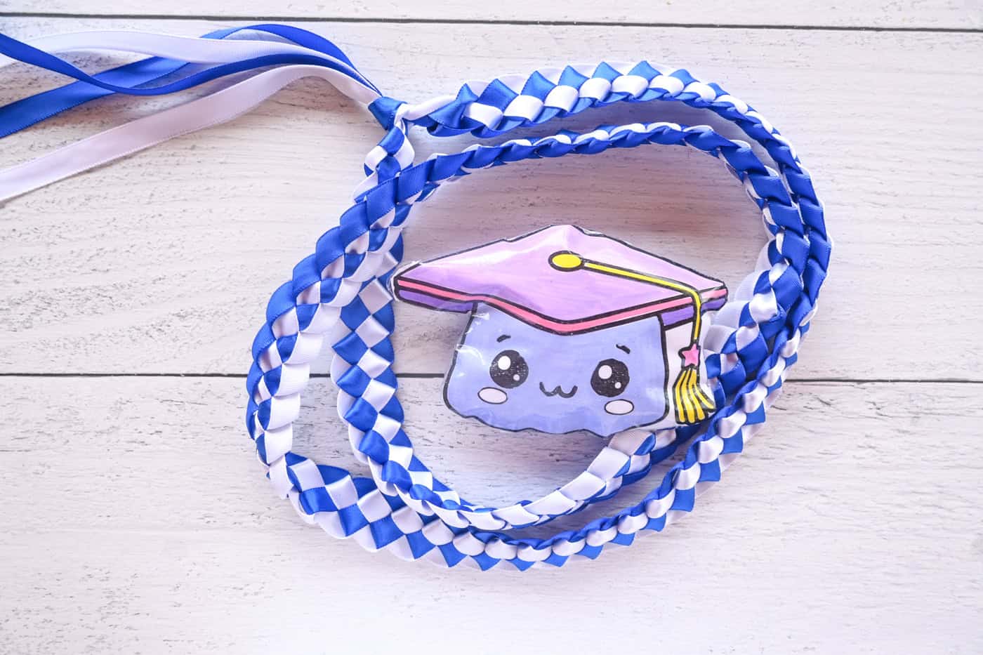 a stop down photo of a paper squishy graduation cap with a blue and white ribbon lei