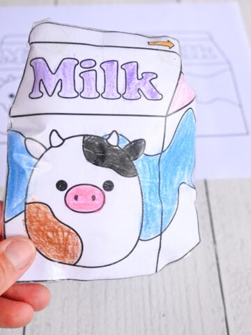 a hand holding a cute milk carton paper squishy in front of a printable paper template for making a IDY paper squishy toy