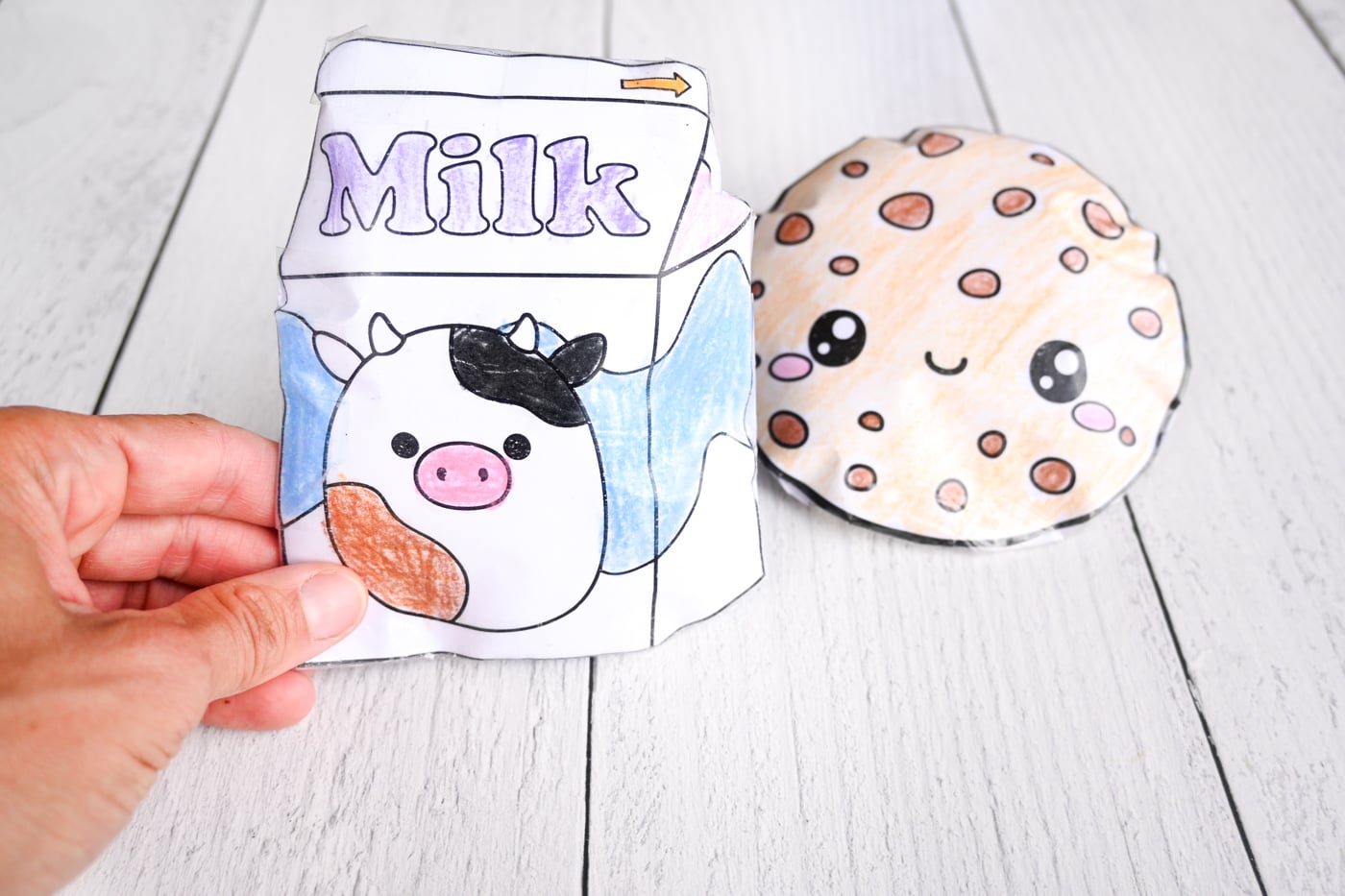 a hand holding a milk carton paper squishy. A cookie paper squishy is visible in the background
