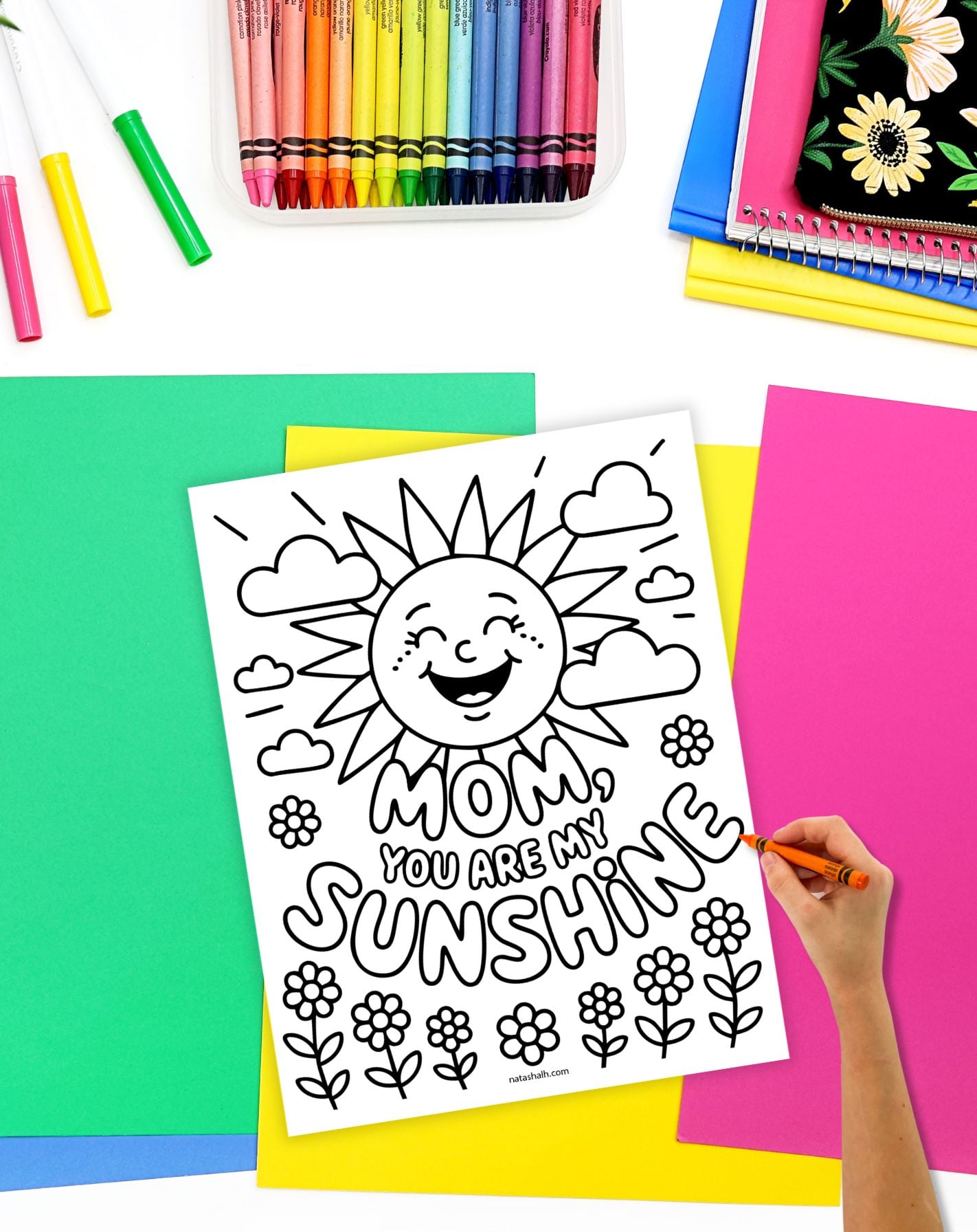a child's hand with a crayon preparing to color a coloring page with "mom, you are my sunshine" and a smiling sun face