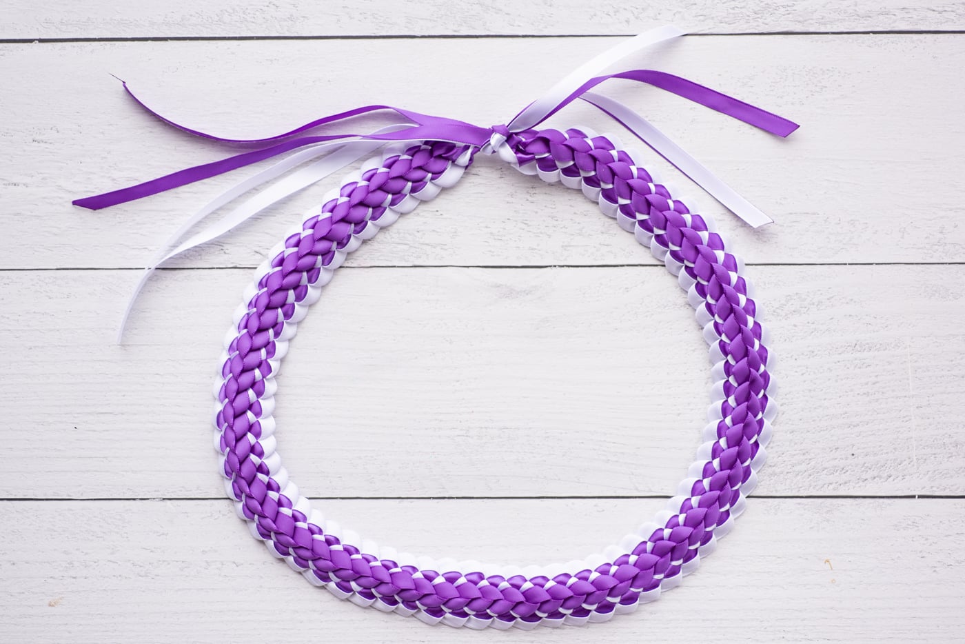a top down photo of a purple and white ribbon lei on a white wood background