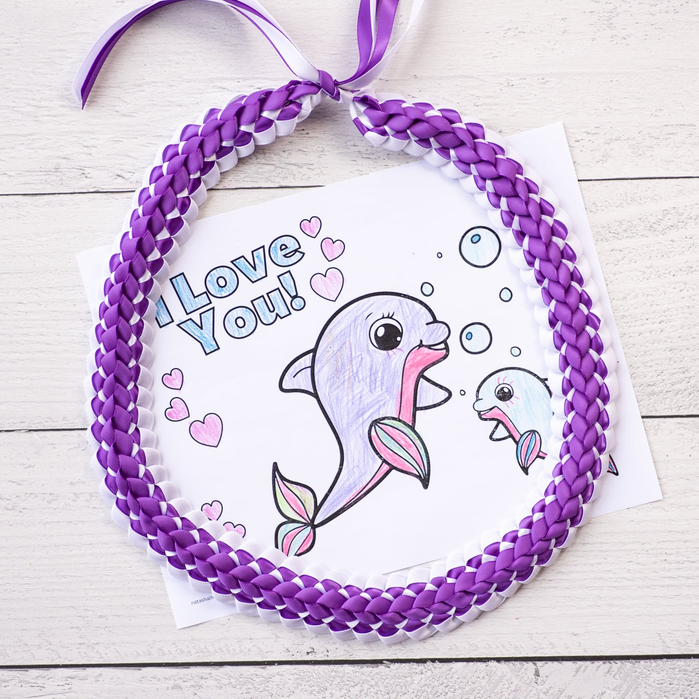 a top down photo of a purple and white double braided Hawaiian ribbon lei with a completed coloring page for Mother's Day 