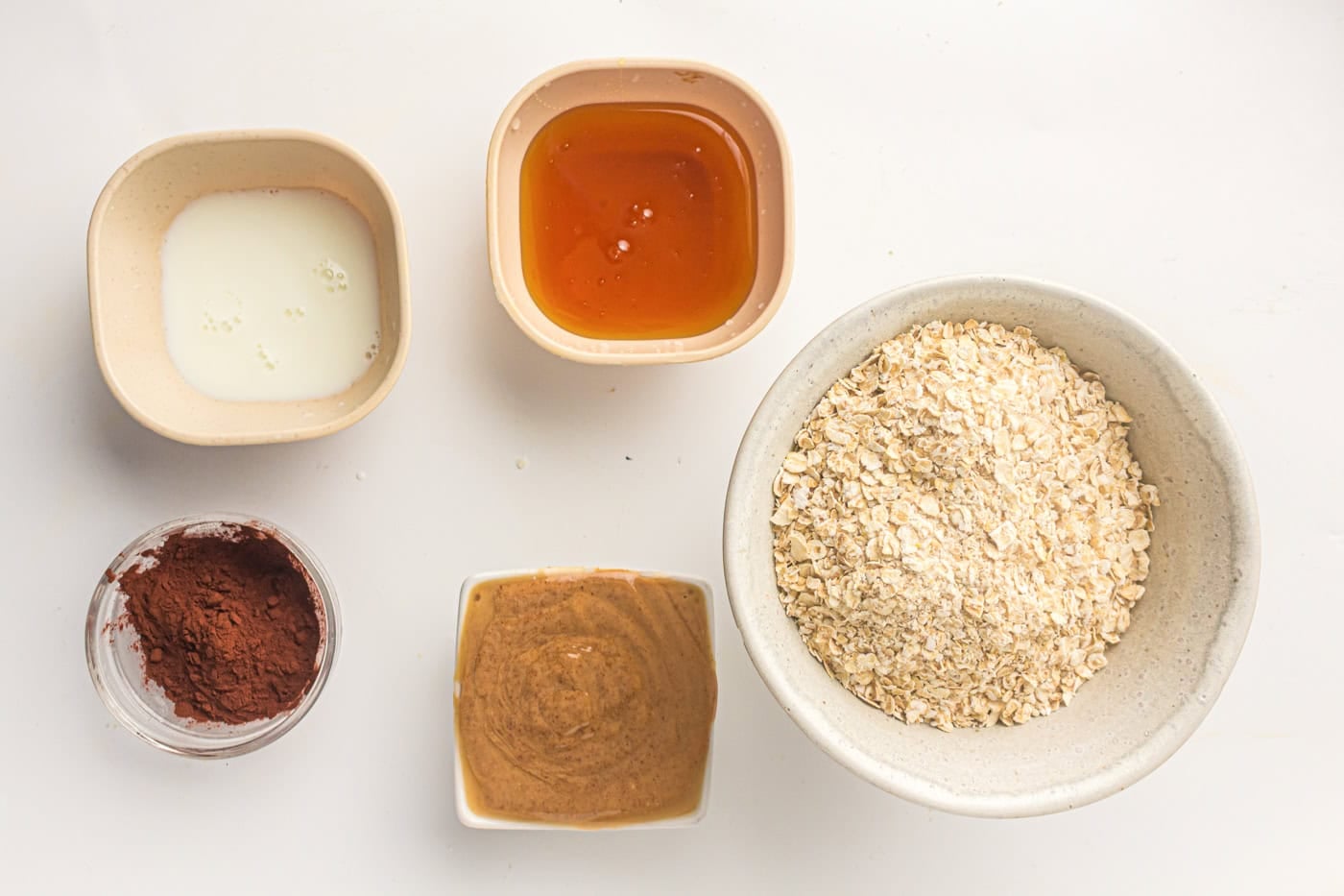 a top down photo of ingredients for no bake oatmeal balls including oatmeal, chocolate powder, peanut butter, milk, and honey