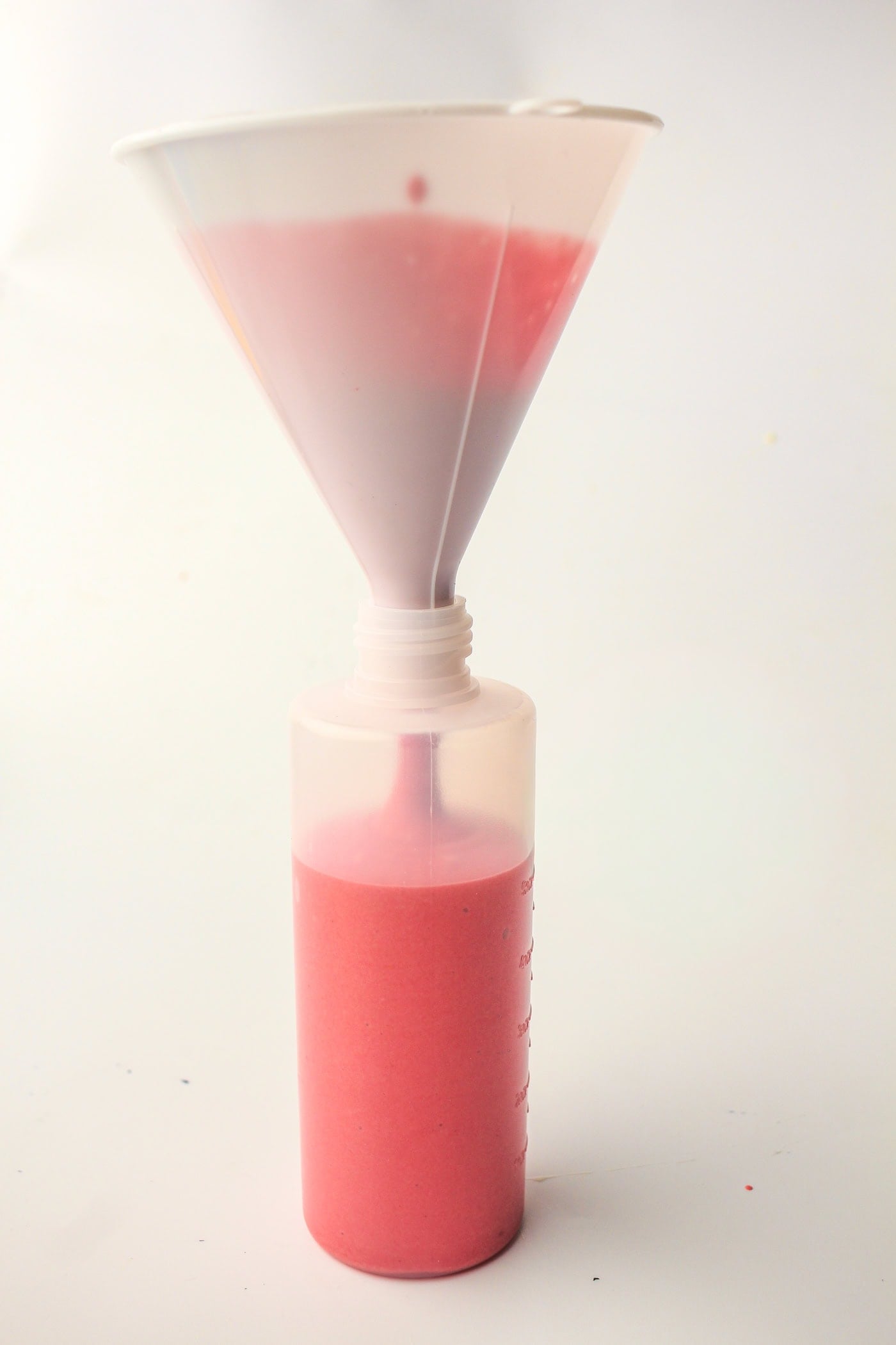 putting homemade red puffy sidewalk paint in a bottle using a funnel