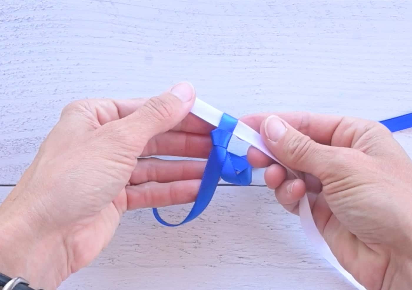 sliding a lop of white ribbon through loop in a blue ribbon