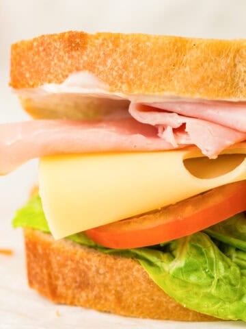 a photo of a thick sandwich made with a sourdough sandwich loaf. The sandwich has Swiss cheese, deli meats, lettuce, and tomato