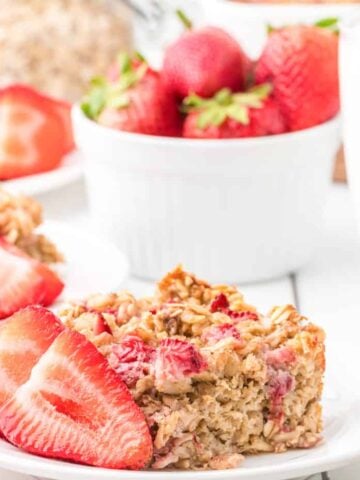 A dish with strawberry baked oatmeal alongside a bowl of strawberries and a glass of milk