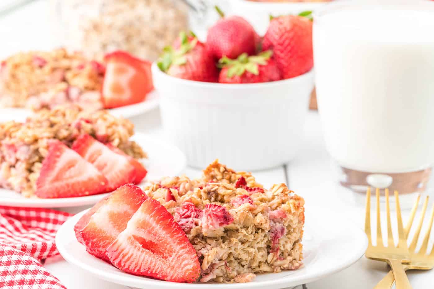 A dish with strawberry baked oatmeal alongside a bowl of strawberries and a glass of milk