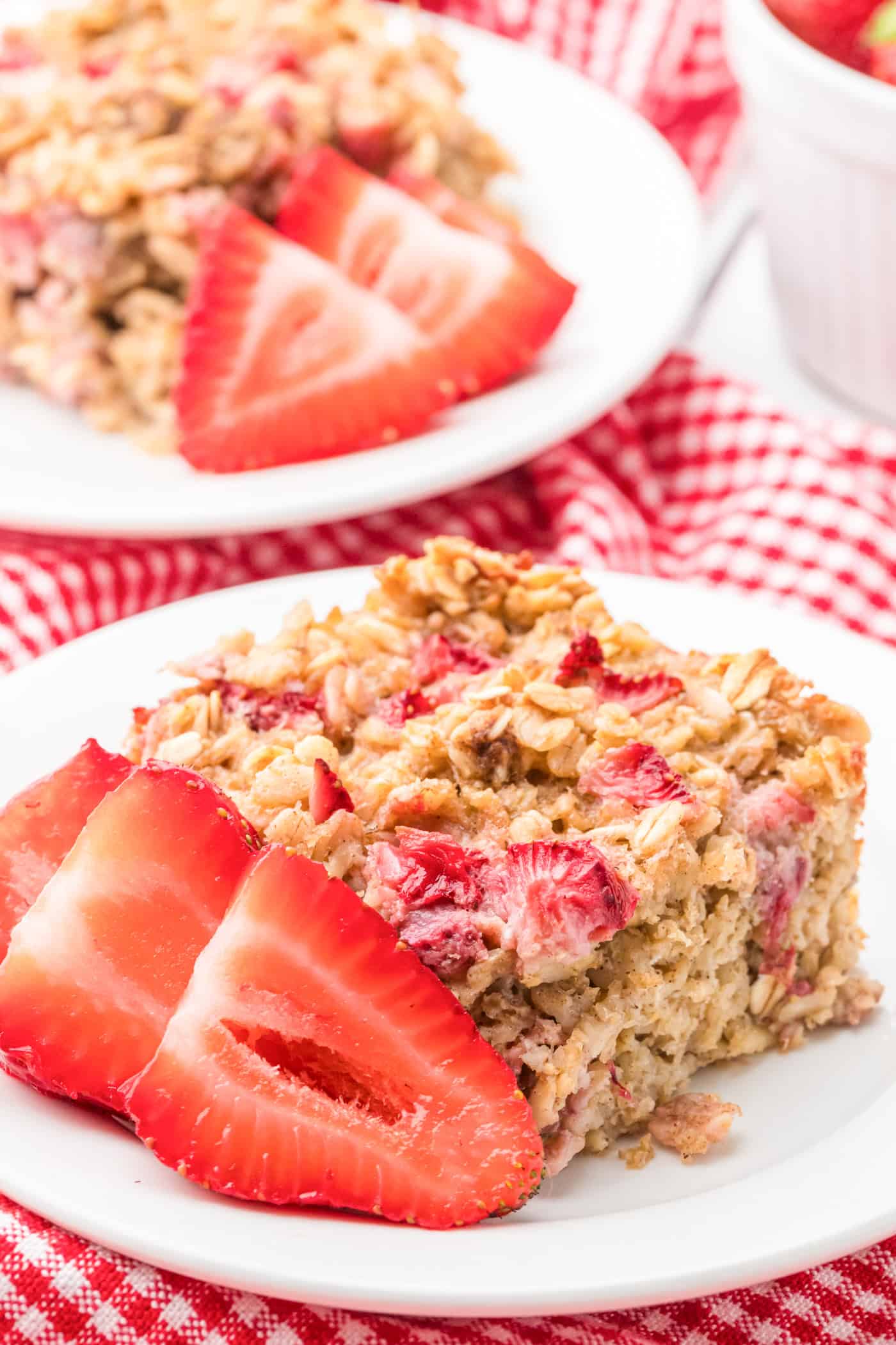 a close in view of a slice of strawberry baked oatmeal with sliced strawberries on small white plate