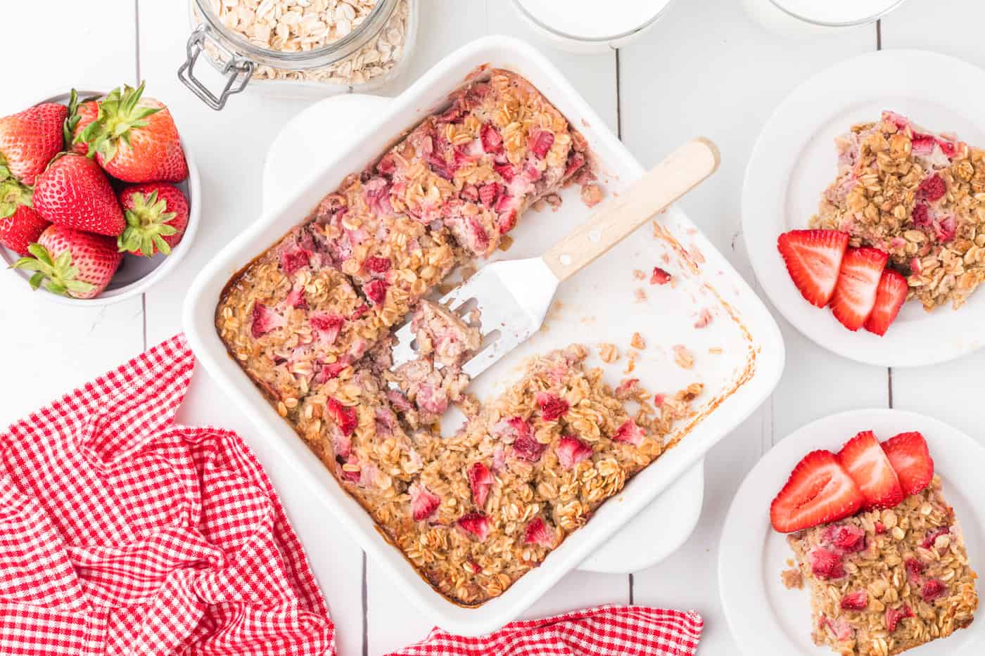 a top down photo of a pan of strawberry baked oatmeal with servings of baked strawberry oatmeal on plates around the outside