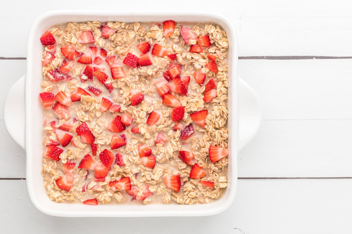 a top down photo of an unbaked dish of strawberry banana baked oatmeal