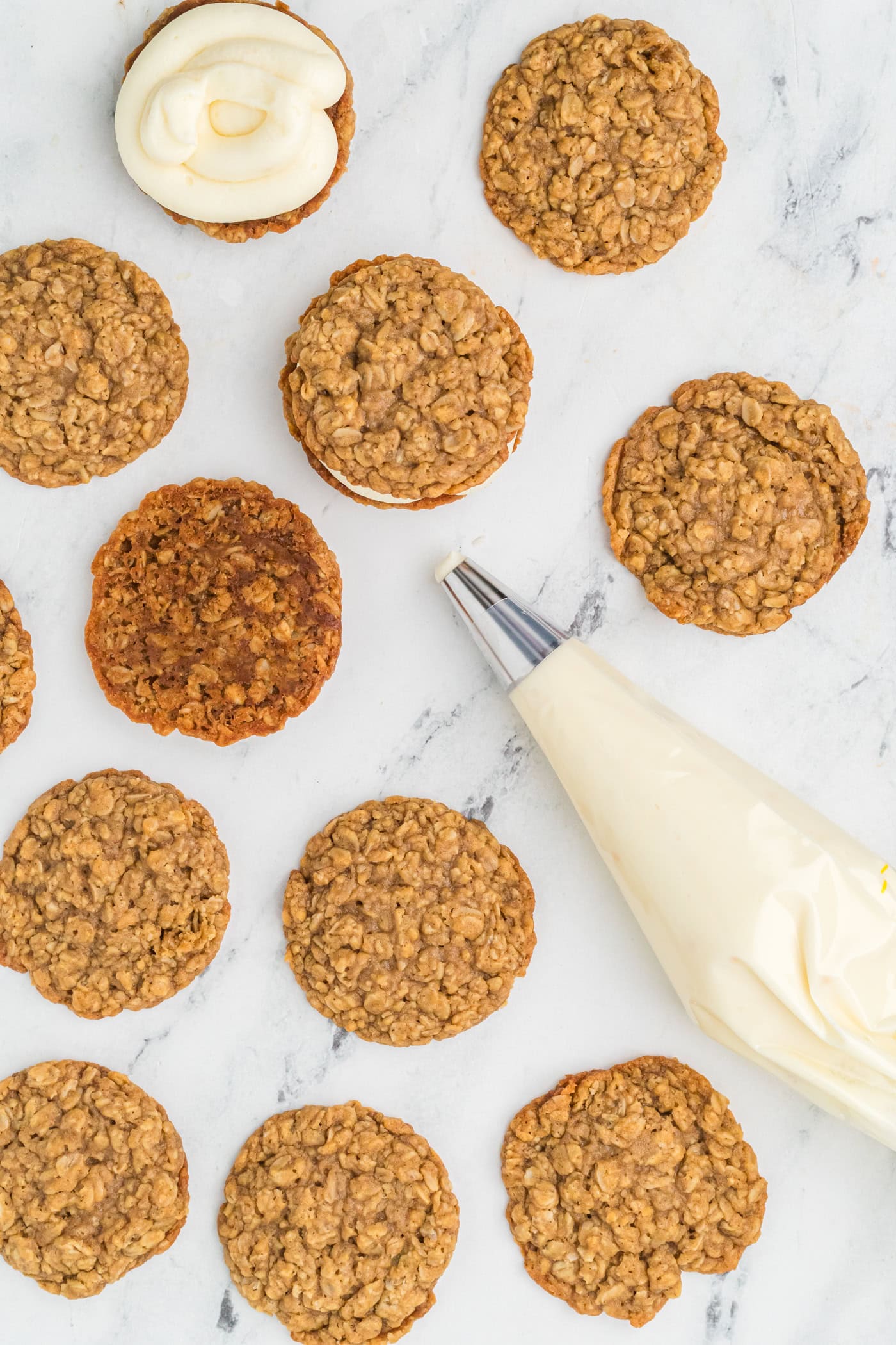 using a frosting bag with buttercream to frost oatmeal cookies for homemade oatmeal cream pies