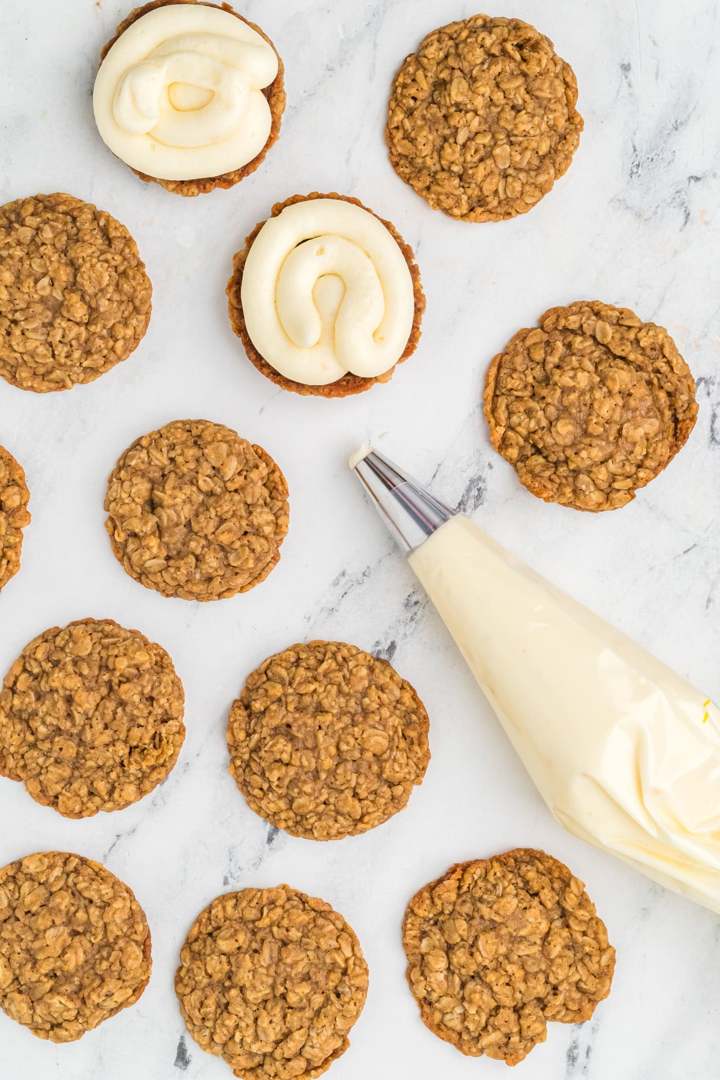 using a frosting bag with buttercream to frost oatmeal cookies for homemade oatmeal cream pies