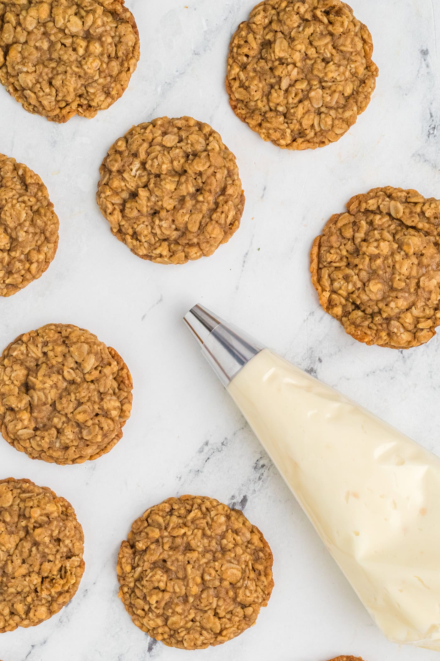 a frosting bag with a tip and buttercream next to oatmeal cookies