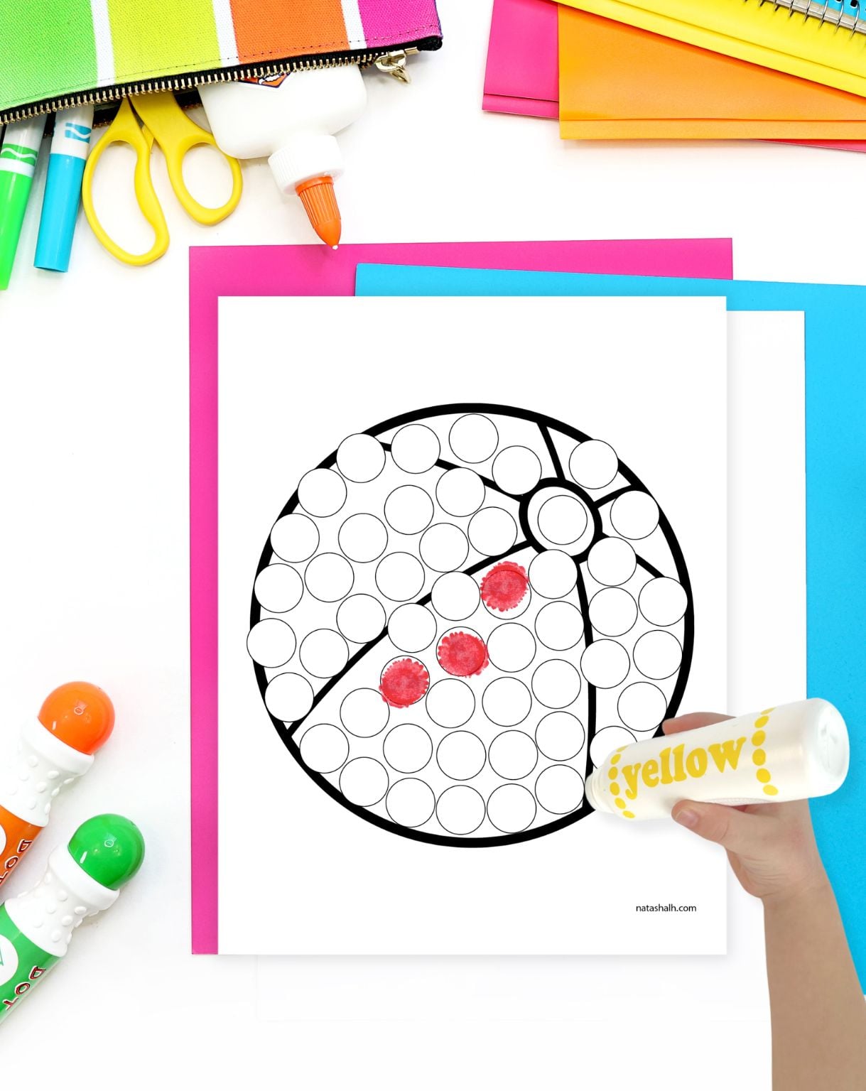 a hand with a yellow dot marker preparing to color a beach ball dauber coloring page