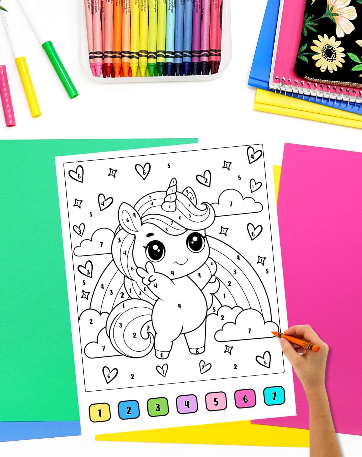 a hand with a crayon preparing to color a unicorn themed color by number sheet with a visual key