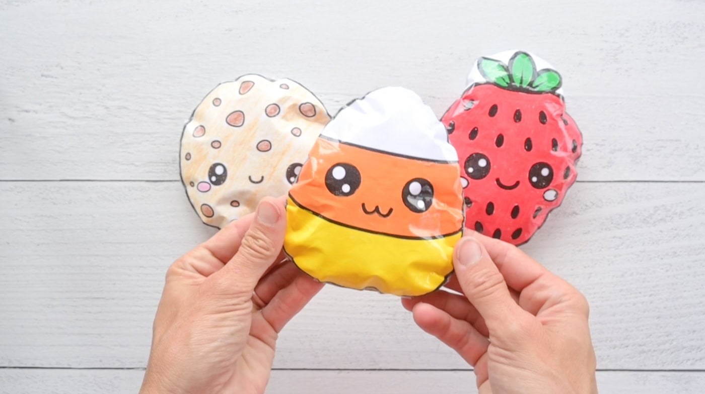 hands holding a paper candy corn squishy. a cookie squishy and a strawberry squishy are visible in the background