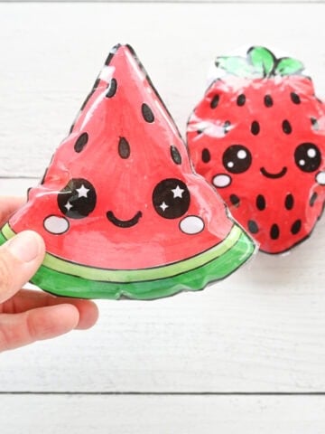 a hand holding a paper squishy watermelon with a strawberry squishy in the background