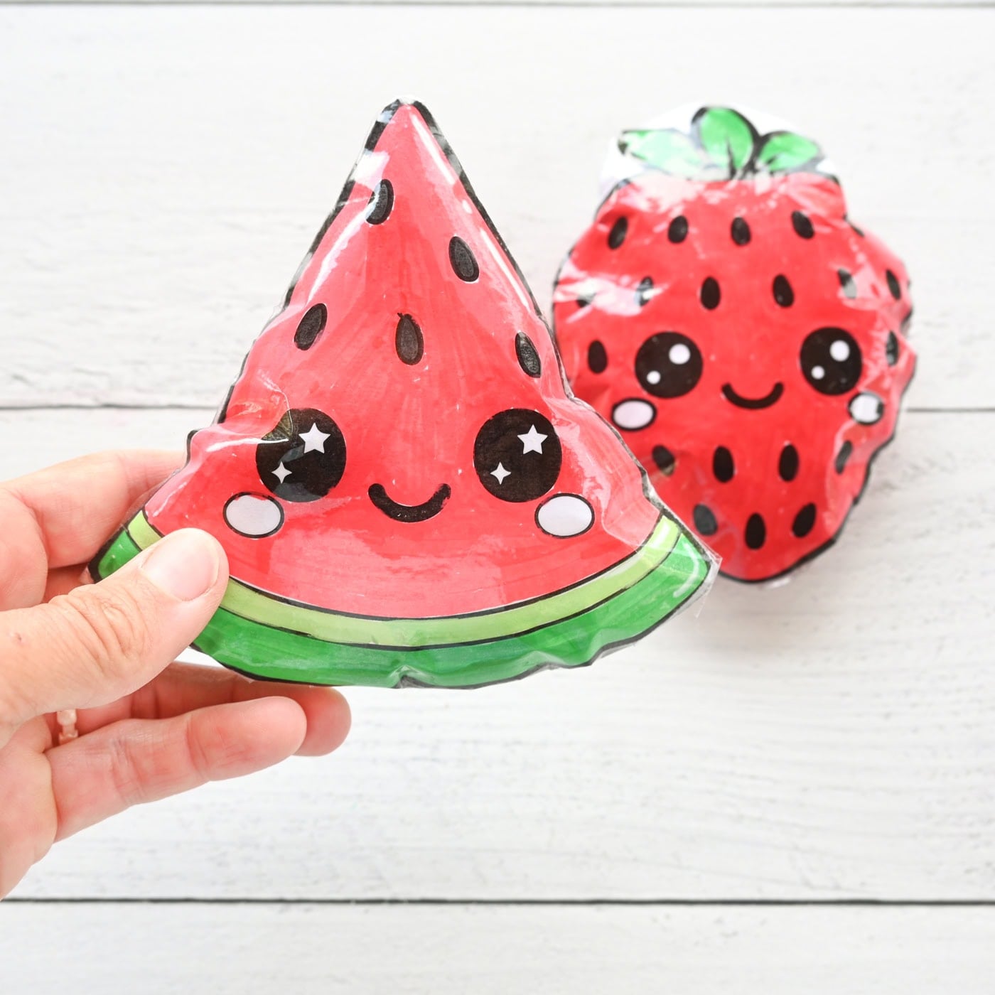 a hand holding a paper squishy watermelon with a strawberry squishy in the background