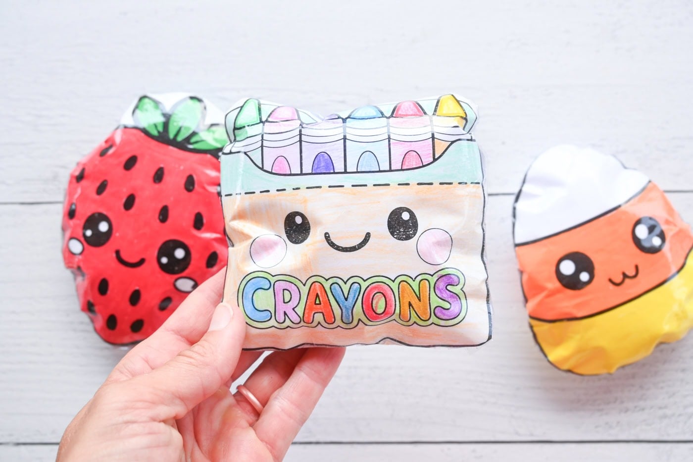 hands holding a kawaii box of crayons paper squishy with a strawberry and a candy corn squishy visible in the background