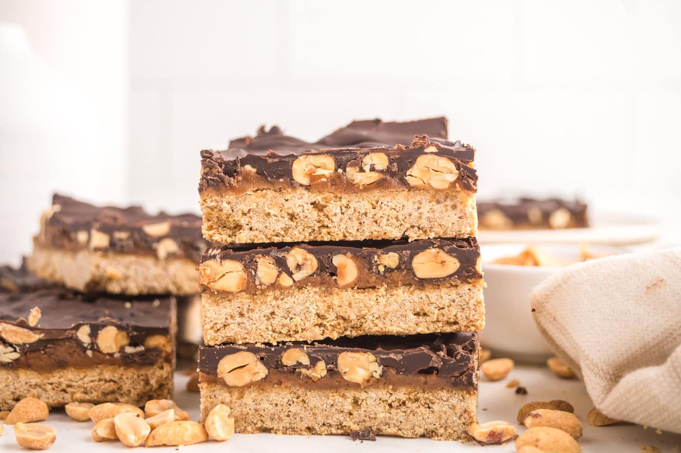 a stack of dairy free healthy snickers bars in front of a bowl with peanuts