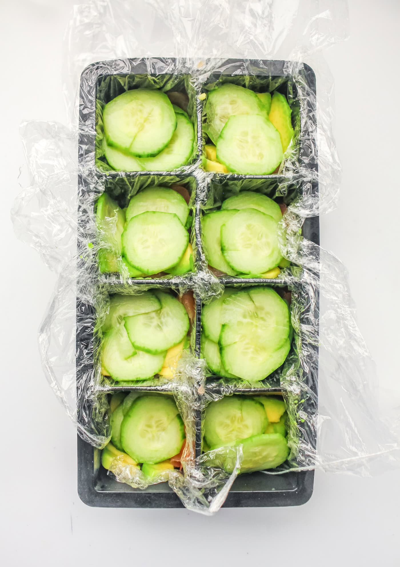 cucumbers placed in each cavity of an ice cube mold to make ice cube tray sushi salmon rolls